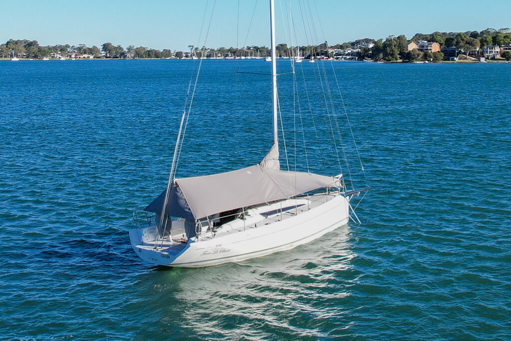 Overall protection cover — three-quarter stern drone view, Italia Yachts 9.98 Bellissima, Lake Macquarie Aerial drone view from the stern quarter of an Italia Yachts 9.98 Bellissima on a mooring in Lake Macquarie fitted with a custom grey WeatherMax overall protection cover by Ocean Covers, Lake Macquarie foreshore in background