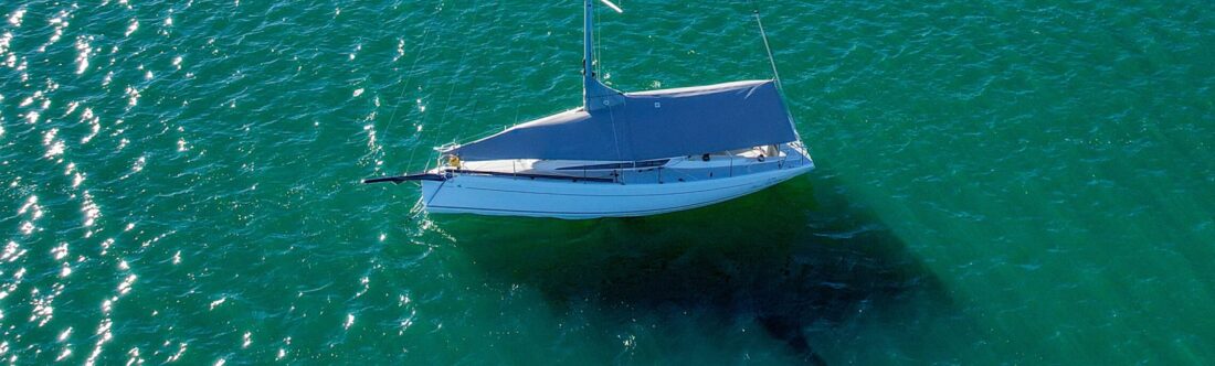 Overhead aerial drone view of an Italia Yachts 9.98 Bellissima on a mooring in Lake Macquarie fitted with a custom grey WeatherMax overall protection cover by Ocean Covers, turquoise water